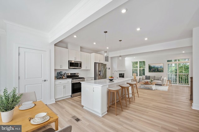 kitchen featuring white cabinetry, a kitchen island with sink, pendant lighting, and appliances with stainless steel finishes