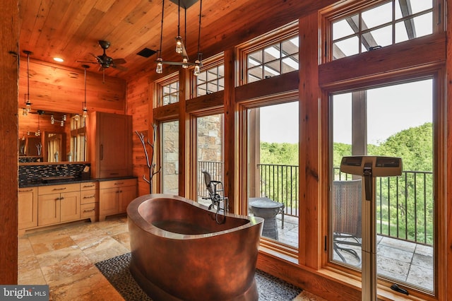 interior space with tasteful backsplash, vanity, ceiling fan, a tub, and wood walls