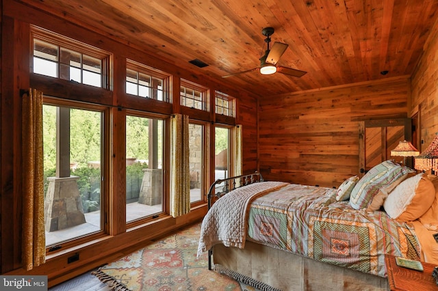 bedroom with hardwood / wood-style floors, ceiling fan, wood walls, and multiple windows