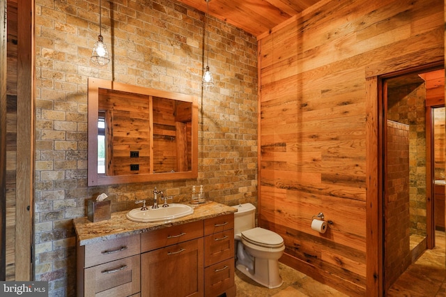 bathroom featuring vanity, toilet, wooden walls, and brick wall