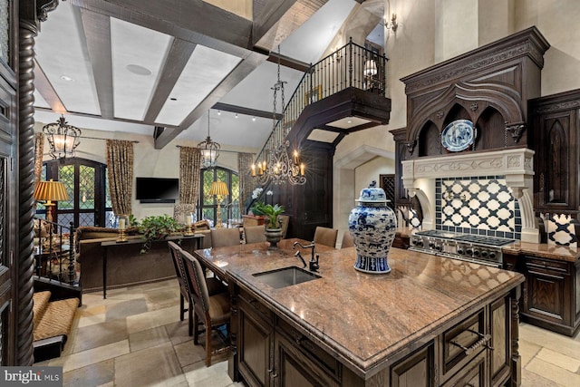 kitchen with a center island with sink, sink, high end stainless steel range, beamed ceiling, and dark brown cabinetry