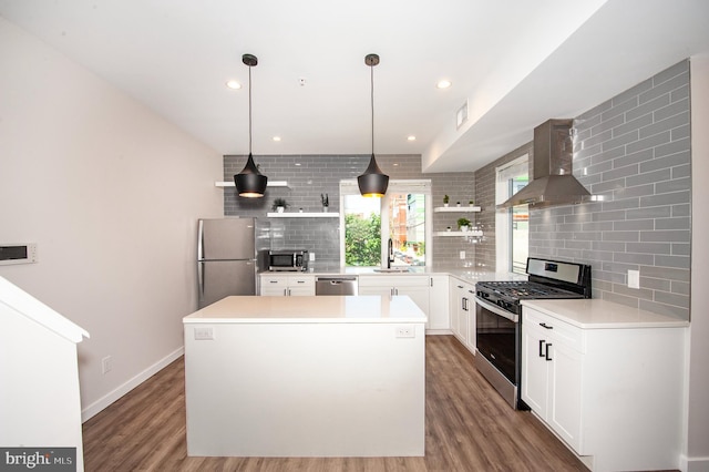 kitchen with appliances with stainless steel finishes, tasteful backsplash, wall chimney exhaust hood, white cabinets, and a center island