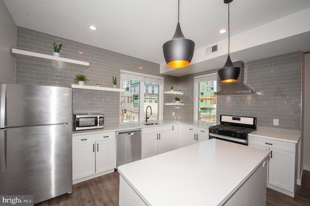 kitchen with pendant lighting, wall chimney range hood, sink, decorative backsplash, and appliances with stainless steel finishes