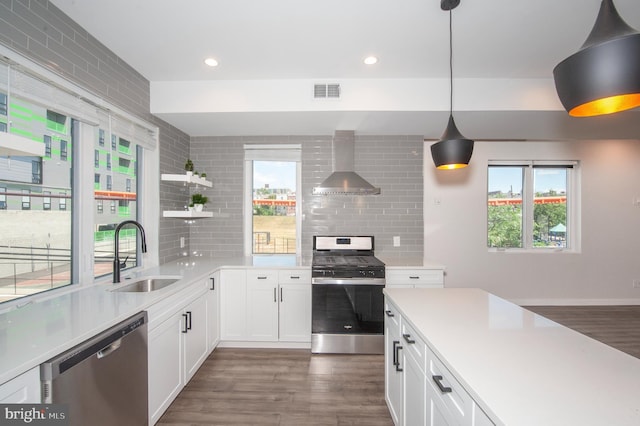 kitchen with sink, wall chimney range hood, decorative light fixtures, decorative backsplash, and appliances with stainless steel finishes