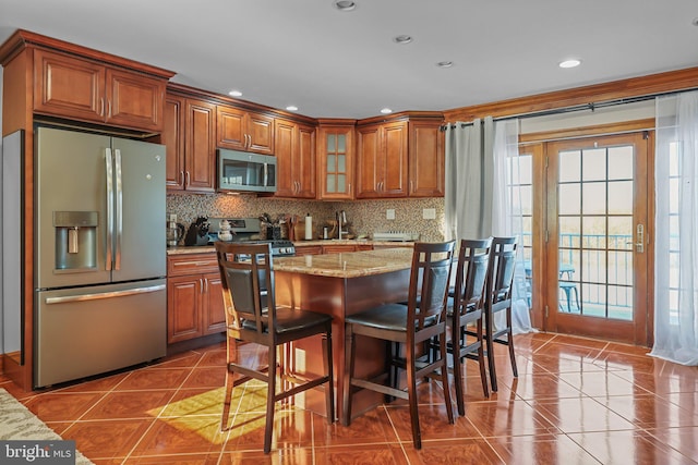 kitchen featuring tile patterned floors, backsplash, light stone counters, and stainless steel appliances