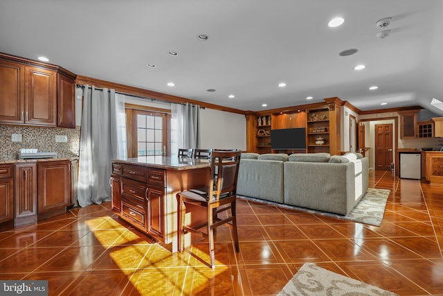 kitchen featuring backsplash, ornamental molding, a breakfast bar, dark tile patterned flooring, and a center island