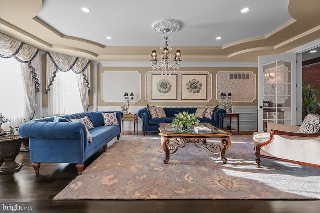 living room with a raised ceiling, crown molding, dark wood-type flooring, and an inviting chandelier