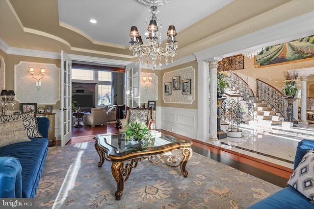 living room with an inviting chandelier, french doors, dark hardwood / wood-style floors, a tray ceiling, and decorative columns