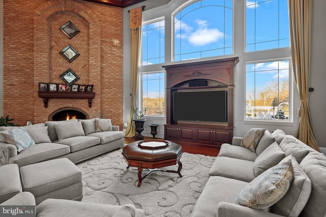 living room with hardwood / wood-style flooring, brick wall, a high ceiling, and a brick fireplace