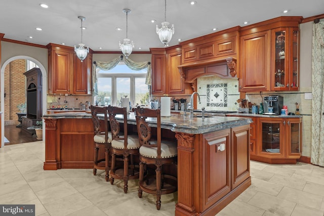 kitchen with pendant lighting, a center island with sink, backsplash, and dark stone counters