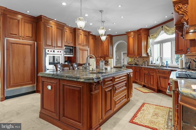 kitchen featuring dark stone counters, stainless steel appliances, sink, pendant lighting, and a center island with sink