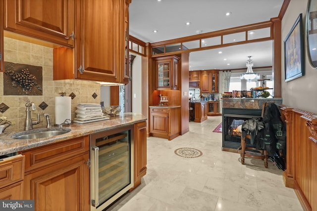 kitchen featuring light stone counters, beverage cooler, crown molding, sink, and a multi sided fireplace