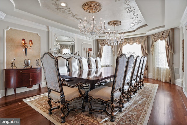 dining space with dark wood-type flooring, crown molding, a tray ceiling, a notable chandelier, and decorative columns