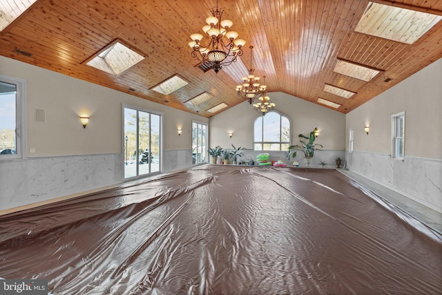 interior space with vaulted ceiling with skylight, plenty of natural light, wooden ceiling, and an inviting chandelier