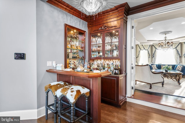 bar featuring dark hardwood / wood-style flooring, ornamental molding, and an inviting chandelier