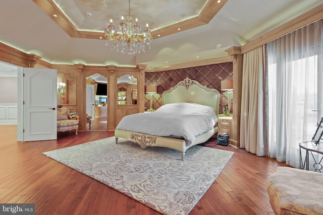 bedroom with a raised ceiling, light wood-type flooring, and an inviting chandelier