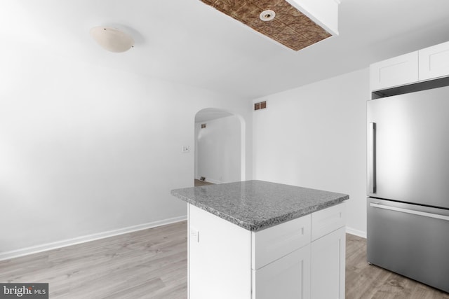 kitchen with white cabinets, stainless steel fridge, a kitchen island, and light wood-type flooring