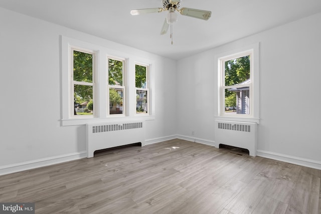 empty room with a wealth of natural light, radiator heating unit, and light hardwood / wood-style flooring