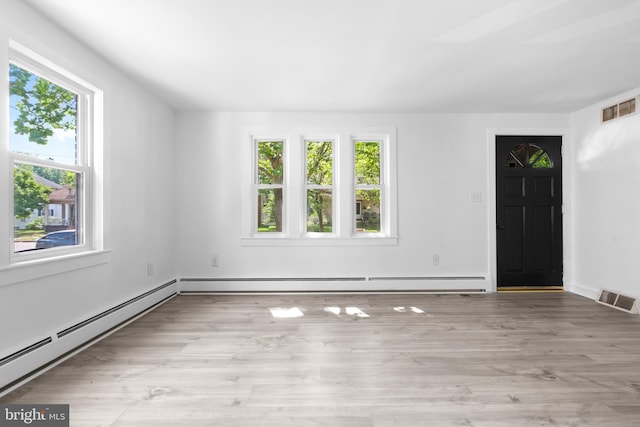 empty room with a healthy amount of sunlight, light hardwood / wood-style floors, and a baseboard heating unit