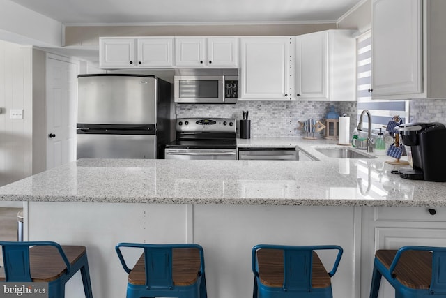 kitchen featuring a kitchen bar, stainless steel appliances, white cabinetry, and sink