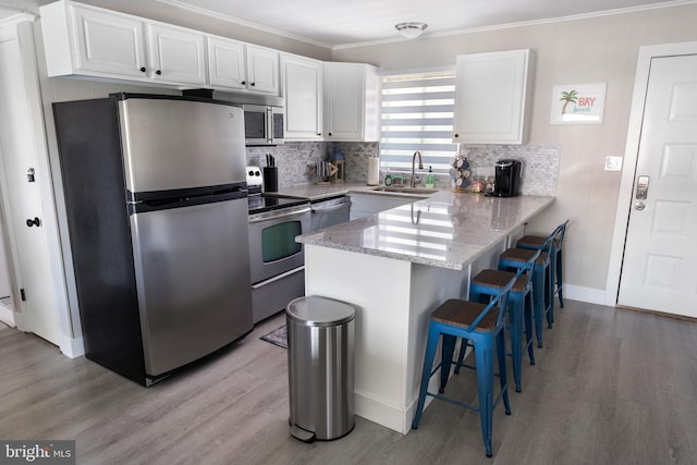 kitchen with white cabinetry, crown molding, light hardwood / wood-style floors, a breakfast bar, and appliances with stainless steel finishes