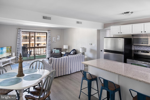 kitchen with light stone countertops, light wood-type flooring, appliances with stainless steel finishes, a kitchen bar, and white cabinetry