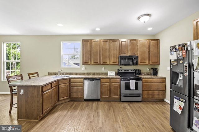 kitchen with a kitchen breakfast bar, sink, light hardwood / wood-style flooring, kitchen peninsula, and stainless steel appliances