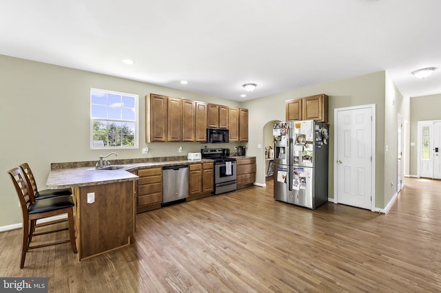 kitchen with kitchen peninsula, appliances with stainless steel finishes, a kitchen breakfast bar, sink, and hardwood / wood-style floors