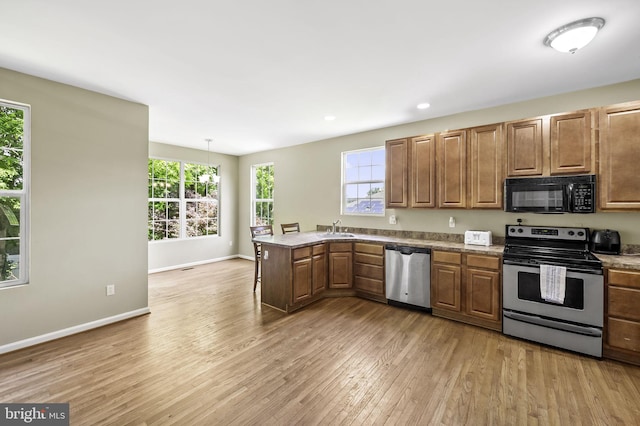 kitchen with pendant lighting, sink, light hardwood / wood-style floors, kitchen peninsula, and stainless steel appliances