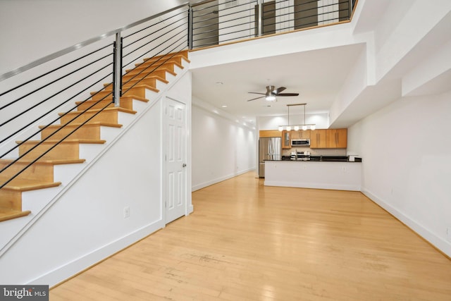 unfurnished living room featuring ceiling fan, light hardwood / wood-style floors, and a high ceiling