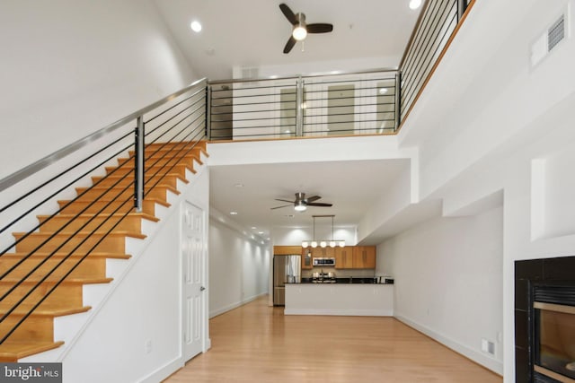 unfurnished living room featuring a fireplace, ceiling fan, light hardwood / wood-style flooring, and a towering ceiling