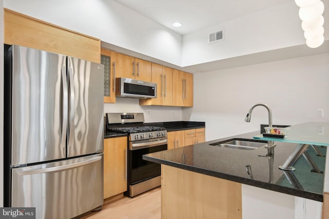 kitchen with sink, dark stone countertops, light wood-type flooring, kitchen peninsula, and stainless steel appliances