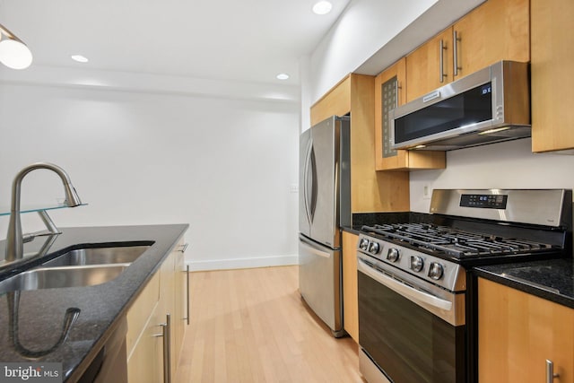 kitchen with stainless steel appliances, light hardwood / wood-style flooring, dark stone countertops, and sink