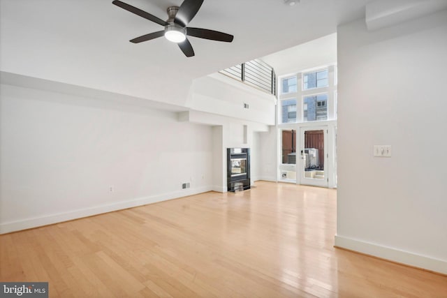 unfurnished living room with a multi sided fireplace, ceiling fan, light hardwood / wood-style flooring, and a towering ceiling