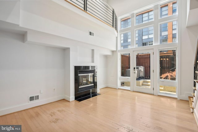 unfurnished living room with a multi sided fireplace, a high ceiling, and light hardwood / wood-style flooring