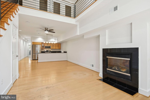 unfurnished living room with a tile fireplace, a towering ceiling, light hardwood / wood-style floors, and ceiling fan