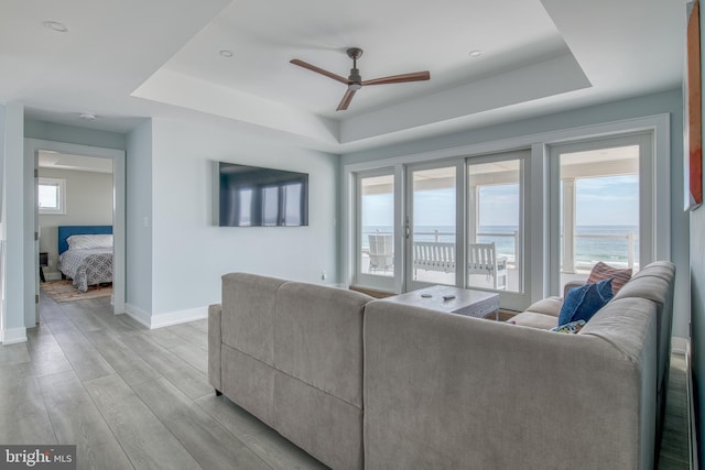 living room with ceiling fan, a tray ceiling, and light hardwood / wood-style flooring