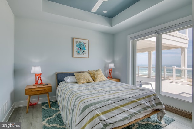 bedroom with hardwood / wood-style floors, a water view, a raised ceiling, and ceiling fan