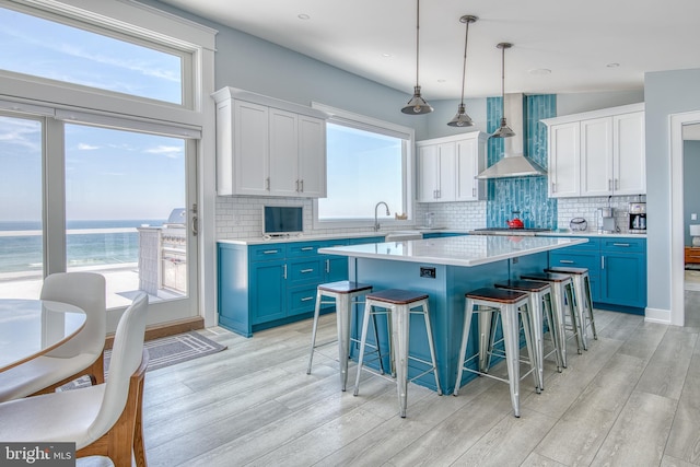 kitchen with decorative backsplash, wall chimney range hood, blue cabinetry, decorative light fixtures, and white cabinets