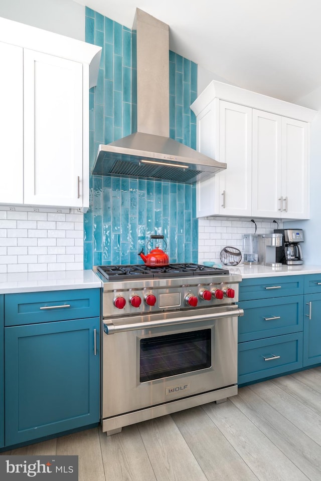 kitchen with decorative backsplash, wall chimney exhaust hood, designer range, light hardwood / wood-style flooring, and white cabinetry