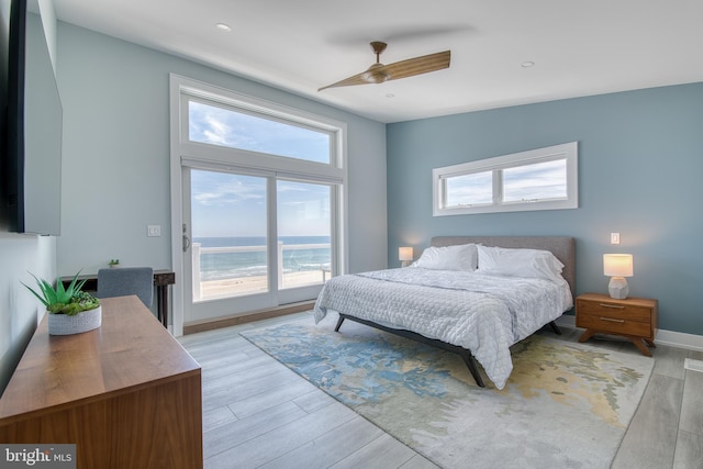 bedroom featuring light wood-type flooring, a water view, multiple windows, and ceiling fan