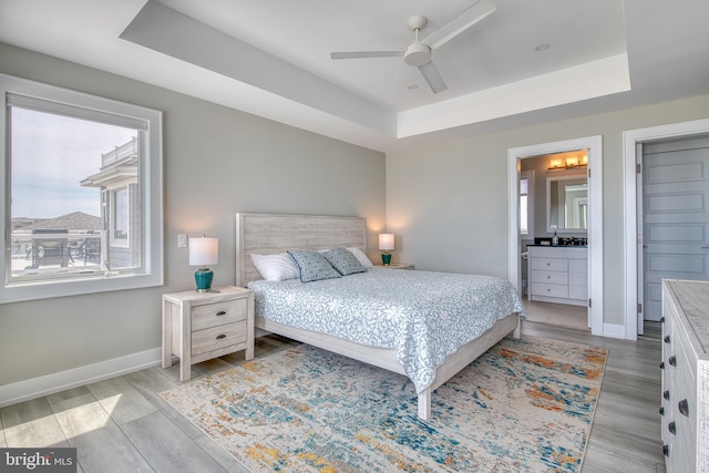 bedroom with hardwood / wood-style floors, connected bathroom, a tray ceiling, and ceiling fan