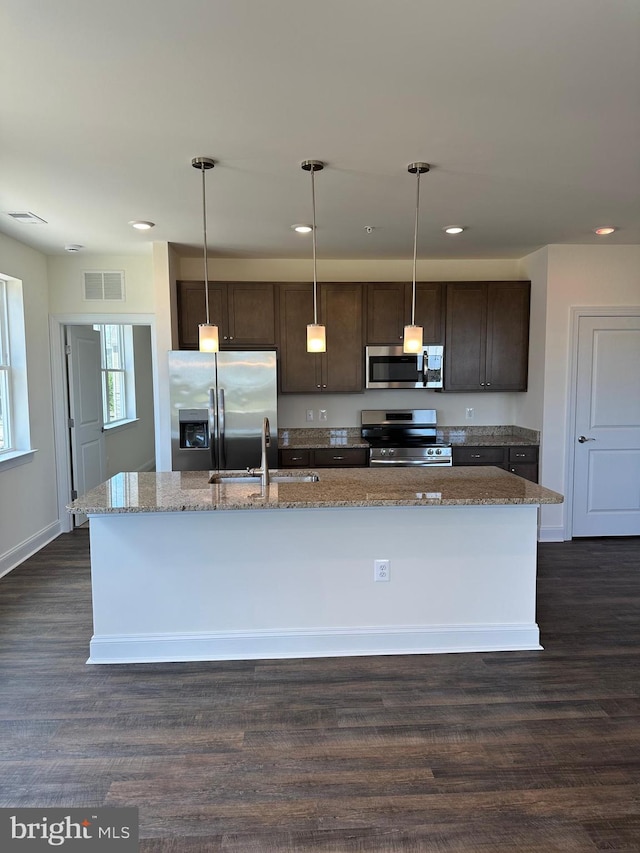 kitchen featuring stainless steel appliances, a kitchen island with sink, dark wood-type flooring, sink, and decorative light fixtures