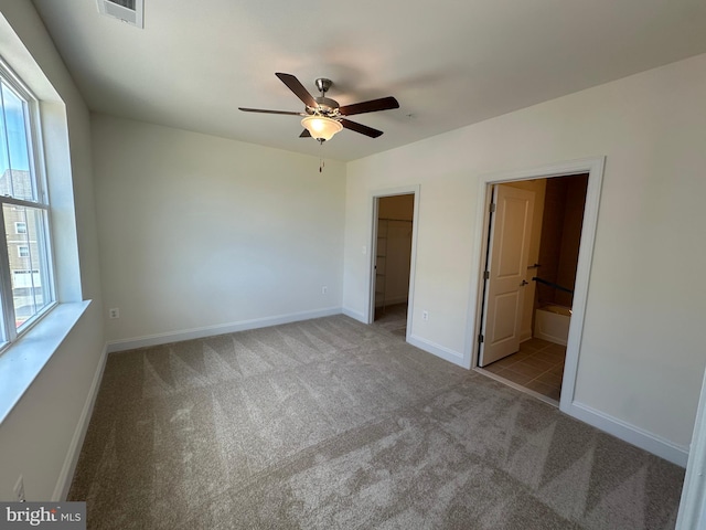 unfurnished bedroom featuring light colored carpet, a walk in closet, connected bathroom, and multiple windows