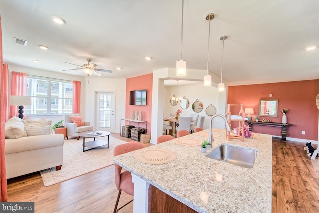 kitchen with light stone countertops, sink, an island with sink, and hanging light fixtures