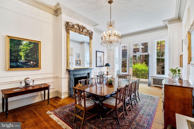 dining area with a notable chandelier, ornamental molding, wood-type flooring, and a fireplace