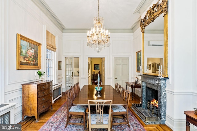 dining room featuring a wall unit AC, crown molding, hardwood / wood-style flooring, a premium fireplace, and an inviting chandelier