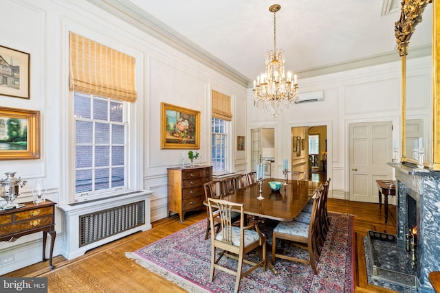 dining room featuring a wall mounted AC, a premium fireplace, hardwood / wood-style floors, crown molding, and a notable chandelier