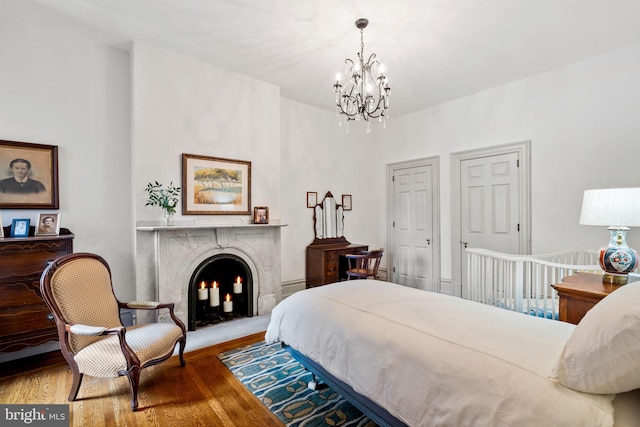 bedroom featuring a notable chandelier, wood-type flooring, and a premium fireplace