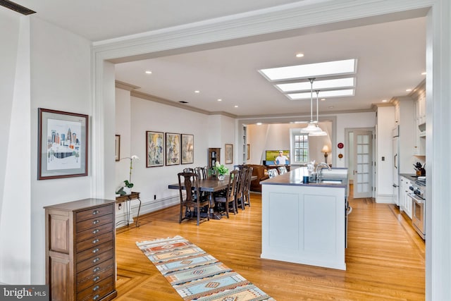 kitchen with white cabinets, a center island with sink, high end stainless steel range oven, pendant lighting, and crown molding